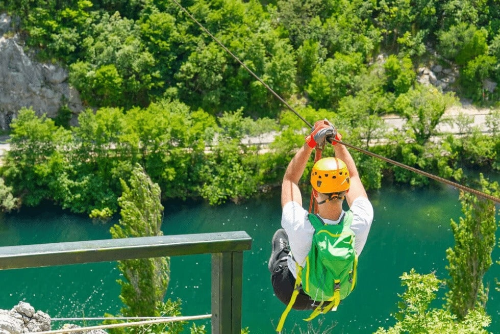 Tripps Now showcases a zip line adventure with views over water, forest, and the natural landscape surrounding the course.